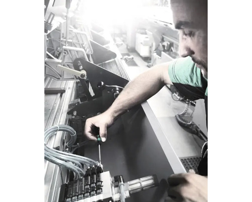 En man som reparerar en maskin med en skruvmejsel.