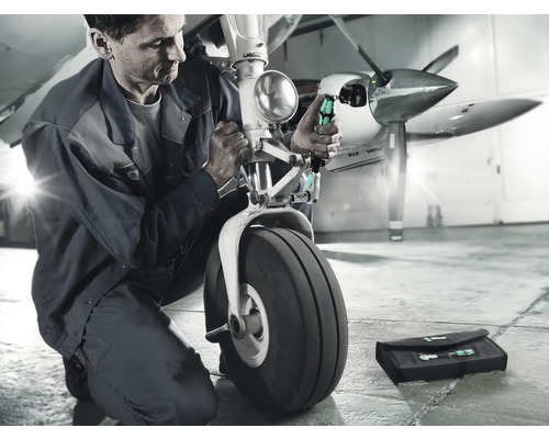 En mekaniker reparerar landningsstället på ett flygplan med skruvmejslar och en verktygsväska.
