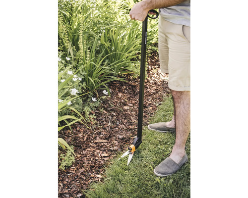 Person klipper gräskanten med en grässax med skaft i trädgården.