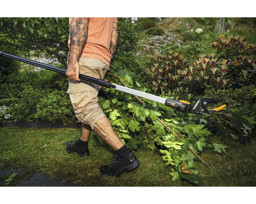 En person beskär grenar i en trädgård med en teleskopisk grensax.