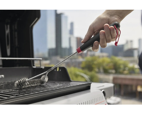 En person rengör ett grillgaller med en grillborste.