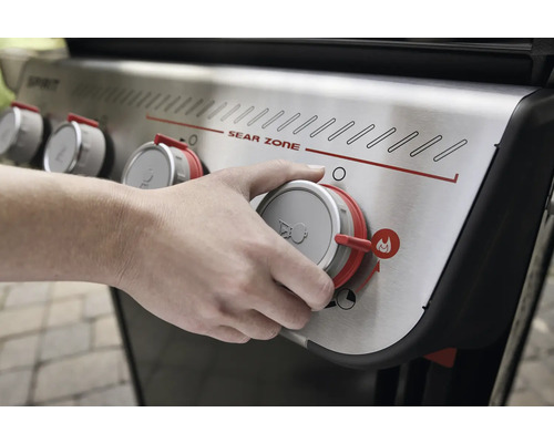 Närbild av en gasolgrill med en hand på vridknappen för att reglera värmen.