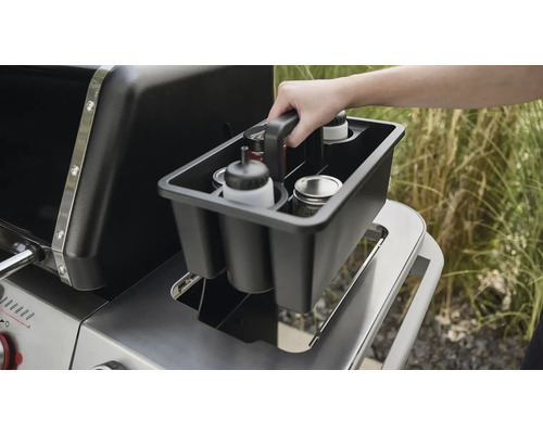 En person placerar en grillbehållare med olika behållare på en grill.