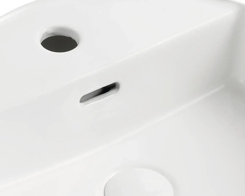 Detaljvy av en vit tvättställ med blandarhål och spillskydd