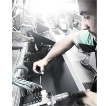 En man reparerar en maskin med en skruvmejsel.