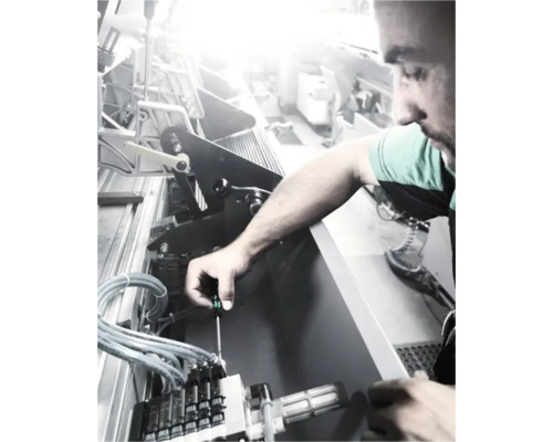 En man reparerar en maskin med en skruvmejsel.