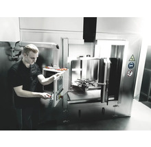 En man använder en industriell rengöringsanläggning i en verkstad. Varningsskyltar indikerar potentiella faror.