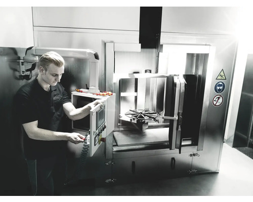 Operatör justerar en industriell rengöringsmaskin för metalldelar.