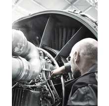 En man reparerar en flygplansturbin med en skruvmejsel.