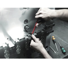 En arbetare utför underhåll på ett metallverktyg med en skruvmejsel.