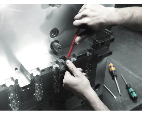 En arbetare utför underhåll på ett metallverktyg med en skruvmejsel.