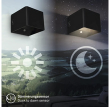 Två svarta kubformade vägglampor som visar övergången från dag till natt med skymningssensor.