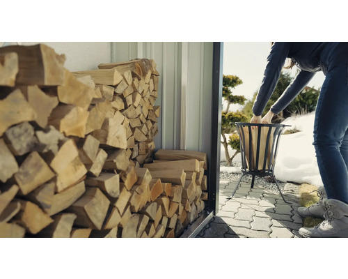 Kvinna fyller eldkorg med ved från en vedbod