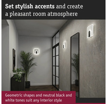 Hall med två geometriska vägglampor, spegel och krukväxt