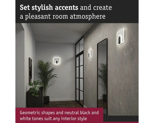 Hall med två geometriska vägglampor, spegel och krukväxt