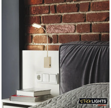 Väggmonterad läslampa bredvid sängen mot en tegelvägg.