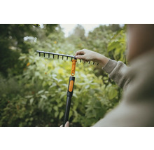 Trädgårdsscen med en person som monterar en lövräfsa på ett skaft.