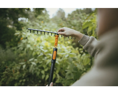 Trädgårdsscen med en person som monterar en lövräfsa på ett skaft.