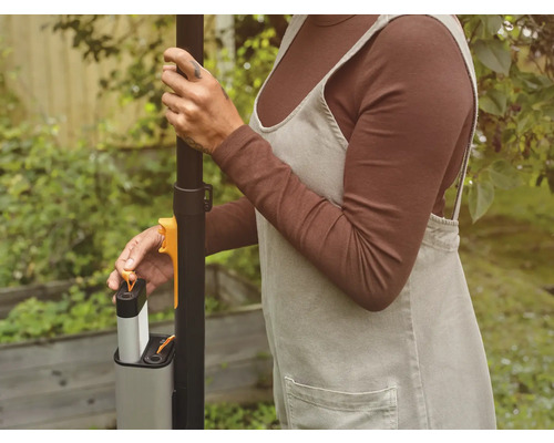 En person sätter i ett batteri i ett trädgårdsredskap.