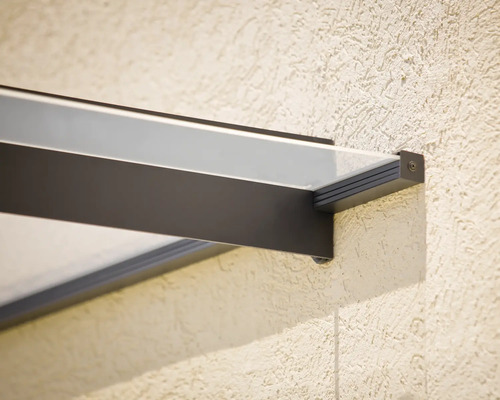 Närbild av ett fäste till ett modernt entrétak i glas med mörk metallram på en strukturerad vägg.