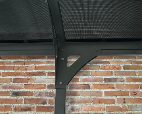 Detaljvy av ett lusthus med polykarbonattak och en stödjande struktur mot en tegelvägg