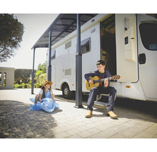 En man spelar gitarr framför en husbil medan ett barn sitter på en uppblåsbar delfin.
