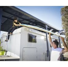 Två personer lyfter en surfbräda på en husbil med markis.