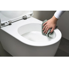 En person rengör en vit vägghängd toalett med en trasa.