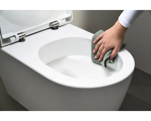 En person rengör en vit vägghängd toalett med en trasa.