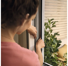 Kvinna installerar ett insektsnät på fönstret.