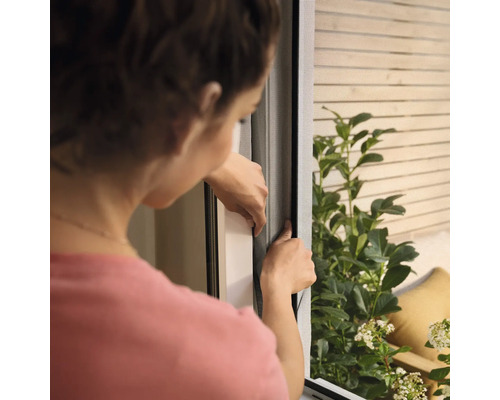 Kvinna installerar ett insektsnät på fönstret.