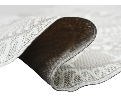 Närbild på en slätvävd matta med geometriskt mönster som visar vävstrukturen och baksidan av det vikta hörnet.