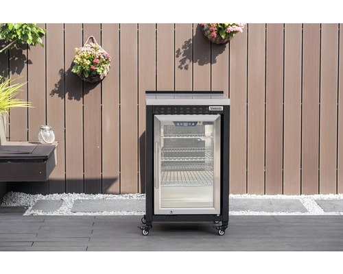 Mobilt Tenneker utomhuskylskåp med glasdörr och hjul på en terrass framför en trävägg.