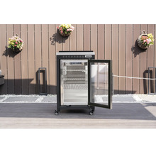 Svart Tenneker utomhuskylskåp med öppen glasdörr och metallhyllor på en terrass framför ett staket.