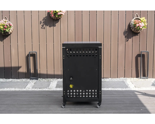 Mobilt underskåp för utekök i svart med ventilationsöppningar och elanslutning på en terrass framför ett trästaket.