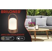Briloner Logo, batteridriven LED-bordslampa på träbord i trädgård med soffa och häck, varmvitt sken 3000 Kelvin, stänkskyddad IP44.