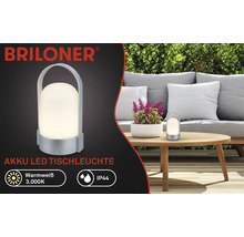 Briloner Logo, batteridriven LED-bordslampa, varmvit 3000 kelvin, IP44, bärbar med bärhandtag, i en trädgård på ett träbord.
