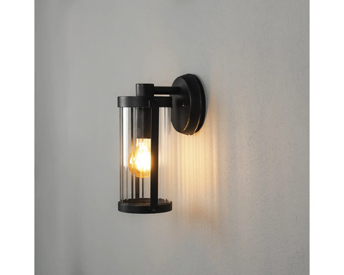 Modern utomhusvägglampa med svart metallram och cylindrisk glasskärm.