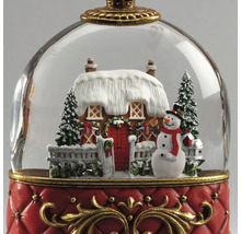 Juldekoration snökula med snötäckt hus, snögubbe och granar på en röd bas med guldfärgade detaljer.
