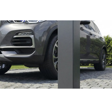 Närbild av en fyrkantig metallstolpe för en carport på en stenlagd uppfart bredvid en grå bil.