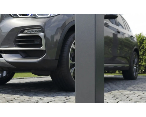Närbild av en fyrkantig metallstolpe för en carport på en stenlagd uppfart bredvid en grå bil.