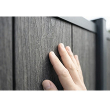 En hand rör vid den strukturerade ytan på en staketpanel med träutseende av trä-plast-komposit.