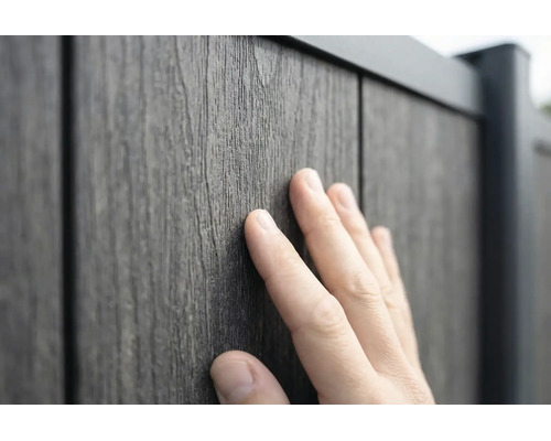 En hand rör vid den strukturerade ytan på en staketpanel med träutseende av trä-plast-komposit.