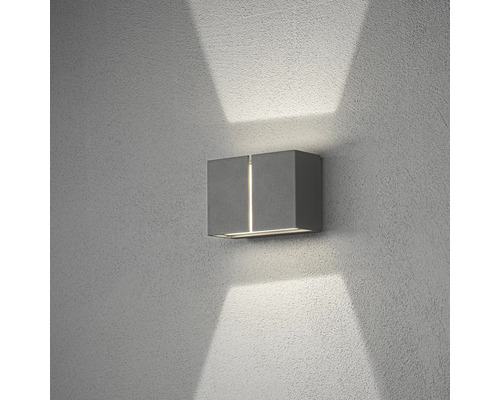 Modern utomhusvägglampa i grått med ljussken uppåt och nedåt på en strukturerad vägg.