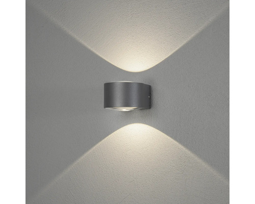 Cylindrisk utomhusvägglampa med ljussken uppåt och nedåt på en strukturerad vägg.