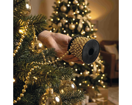 Hand som håller en rulle med pärlgirland vid dekorering av en julgran med julgranskulor och belysning.