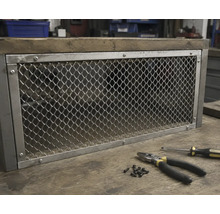 Metallnät i metallram monterat på en trästomme i industriell design, på en arbetsbänk med tång, skruvmejsel och skruvar.
