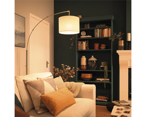 Modern golvlampa med tygskärm bredvid en ljus soffa i ett ombonat vardagsrum med en mörk bokhylla.