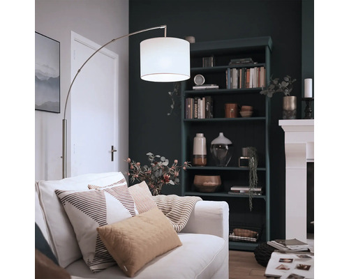 Modern båglampa med tygskärm och metallstativ i ett mysigt vardagsrum med bokhylla och öppen spis.