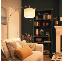 Modern golvlampa med tygskärm bredvid en soffa i ett mysigt inrett vardagsrum med en mörk bokhylla och en öppen spis.